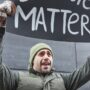 A man protests with a sign outdoors in winter attire, expressing a powerful message.