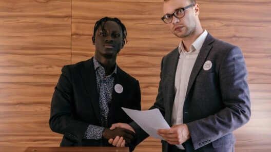 Two men in business attire shaking hands with agreement, promoting voting indoors.