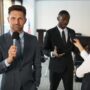 A journalist interviews a businessman in a conference room, capturing a professional and political setting.