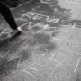 Person writing protest message with chalk on streets of NYC, urging budget revision.