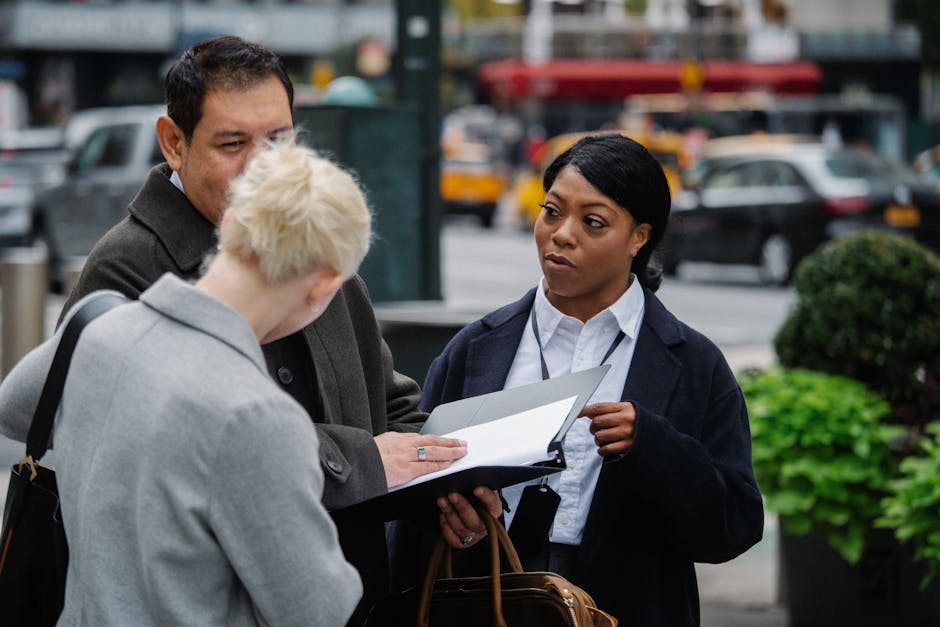 Three professionals discussing documents on a busy city street, showcasing teamwork and collaboration.