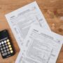 Top view of tax documents, calculator, and coins on wooden table.