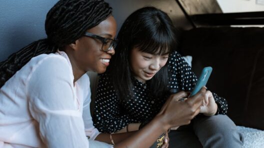 Two women relaxed on a sofa, sharing and enjoying moments on a smartphone.