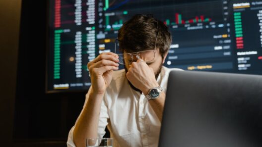 A stressed man looks at stock market data on his computer screen in an office setting.