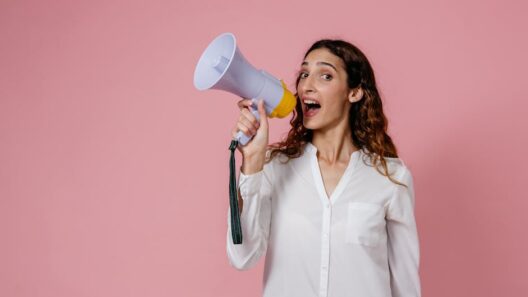 Woman in white shirt holding megaphone against a pink background, confidently speaking.