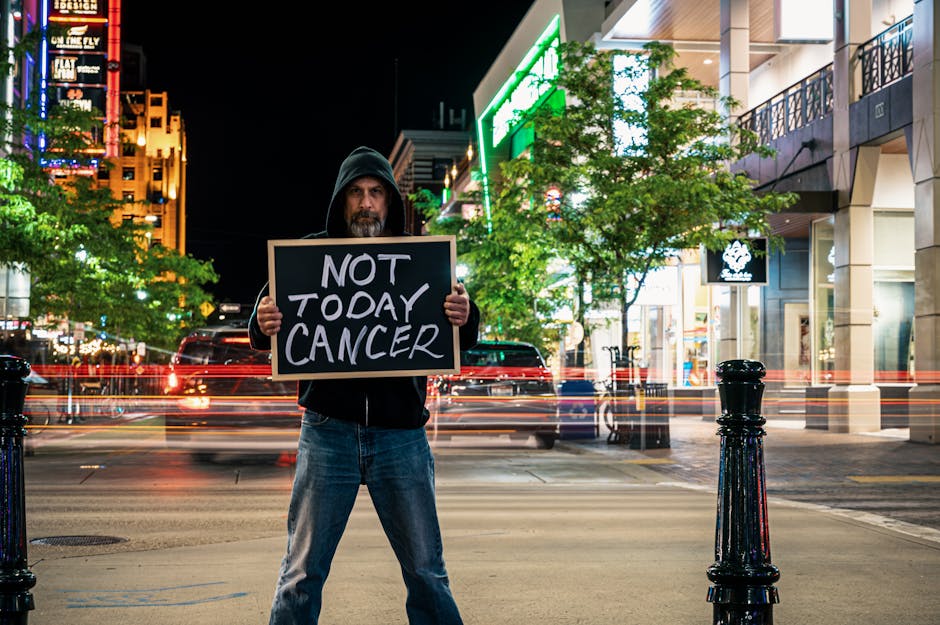 Man holds anti-cancer sign in a busy urban night setting, with light trails and buildings.