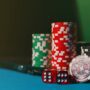 Close-up of casino chips and dice on a felt table, next to a laptop for online gambling.