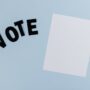 Flat lay of blank paper with 'VOTE' letters on light blue background, ideal for election-themed content.